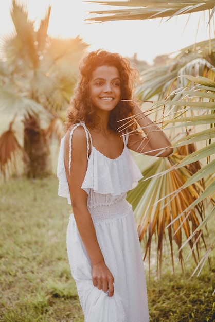 Beautiful girl smiling near palm trees in a white dress