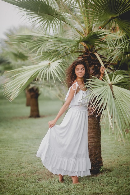 Beautiful girl smiling near palm trees in a white dress