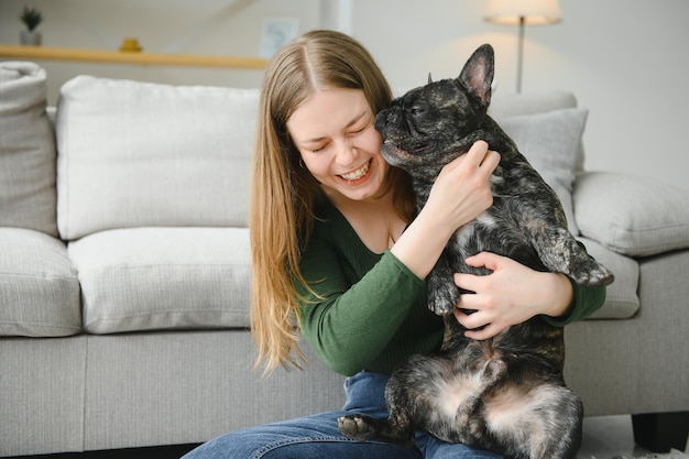 Beautiful girl smiling and sitting on floor near French bulldog