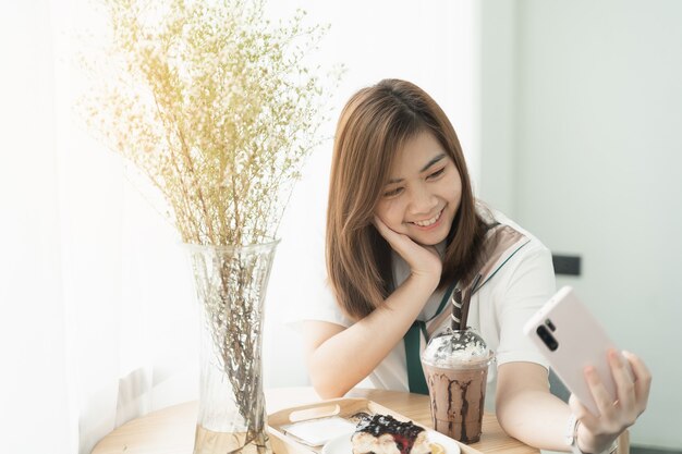 Bella ragazza che sorride usando il selfie del cellulare al bar, la ragazza mangia caffè e torta
