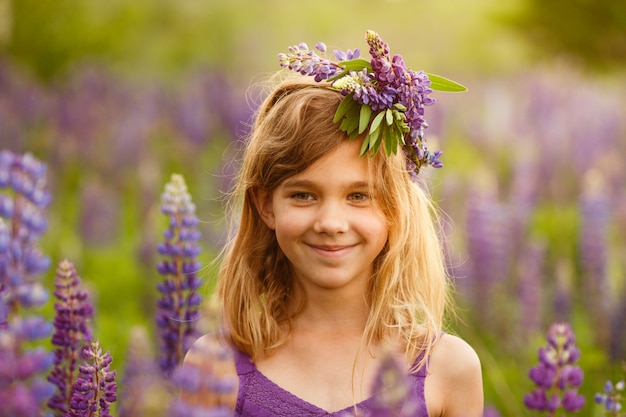 Beautiful girl smiling in a violet dress with a wreath of lupines