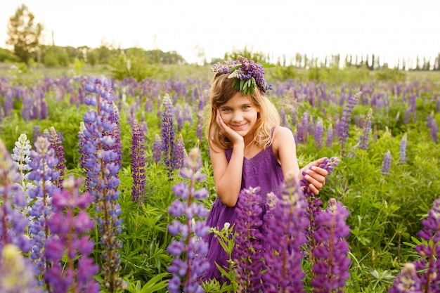 ルピナスの花輪と紫のドレスで笑っている美しい女の子