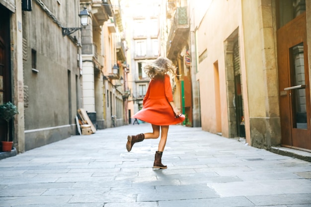 旧市街で回転する美しい女の子ヒップスター旅行幸せな観光客のダンスオレンジ色のスタイリッシュなドレスの女性風の髪