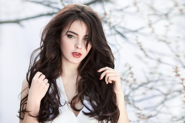 Beautiful girl standing at blossoming tree in the garden over white