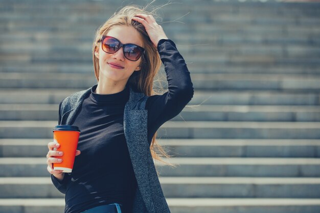 写真 コーヒーとメガネを持って通りに立っている美しい少女。