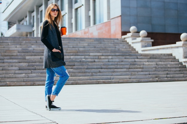 Bella ragazza in piedi sulla strada con caffè e bicchieri.