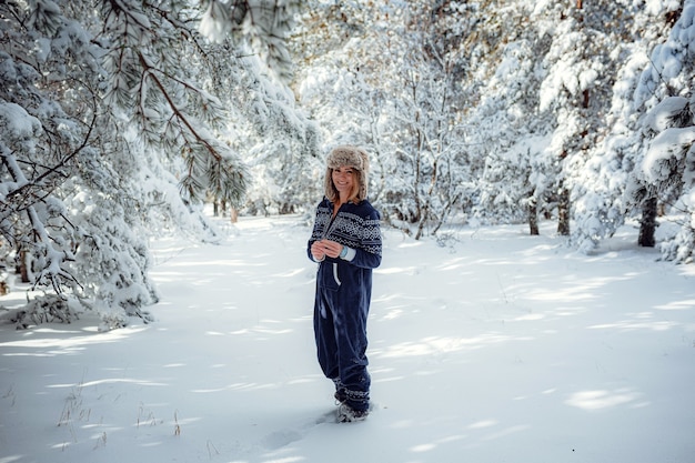 立っている美しい少女、森の公園で冬、クリスマスツリーの雪の背景、彼女はリゾートで休んでいます。テキスト用の空き容量。スポーツ用の青いジャンプスーツ。