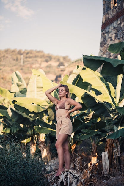 A beautiful girl stands in a beautiful pose near a palm tree portrait shooting on a banana plantation