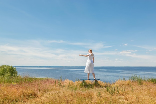 美しい少女が空を眺めながら海岸のベンチに立つ