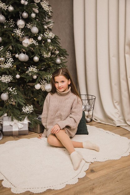 A beautiful girl stands near a Christmas tree with a gift