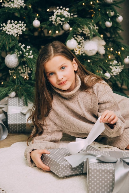 A beautiful girl stands near a Christmas tree with a gift