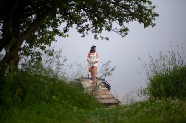 Beautiful girl stands on the pier by the river