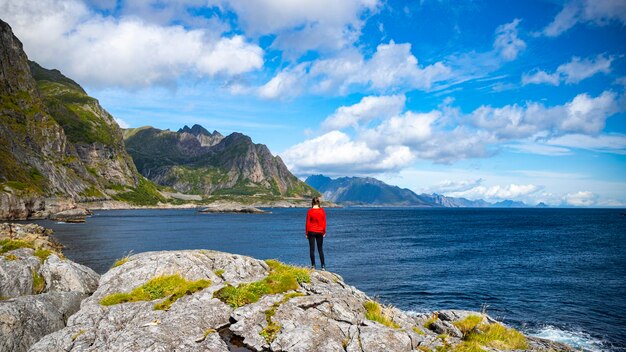 A beautiful girl stands on the rocks above the sea overlooking the mighty mountains on the lofoten i