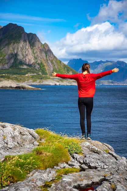 A beautiful girl stands on the rocks above the sea overlooking the mighty mountains on the lofoten