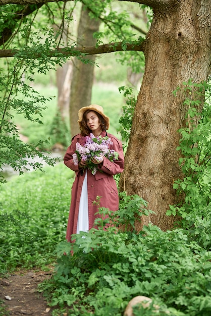 Beautiful girl in a straw hat in the forest Girl with lilac flowers in spring time