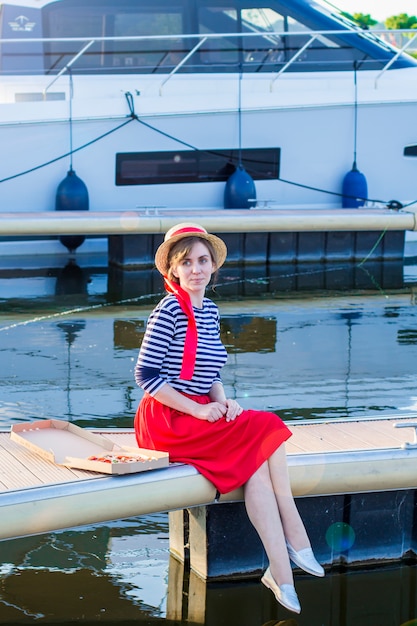 Beautiful girl in a straw hat on the pier near the sea yachts and boats.