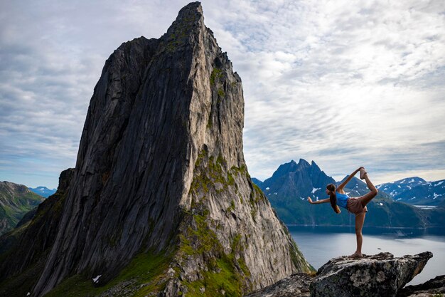 beautiful girl stretches (yoga - dancer position) on rocks overlooking famous segla mountain, norway