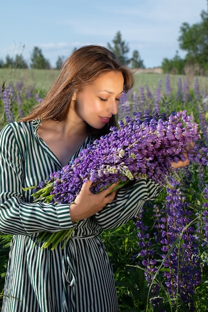 咲くフィールドでルピナスの花の香りがする縞模様の夏のドレスの美しい少女