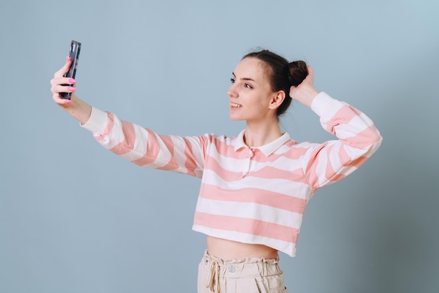 A beautiful girl in a striped sweater takes a selfie on a blue background and buns on her head