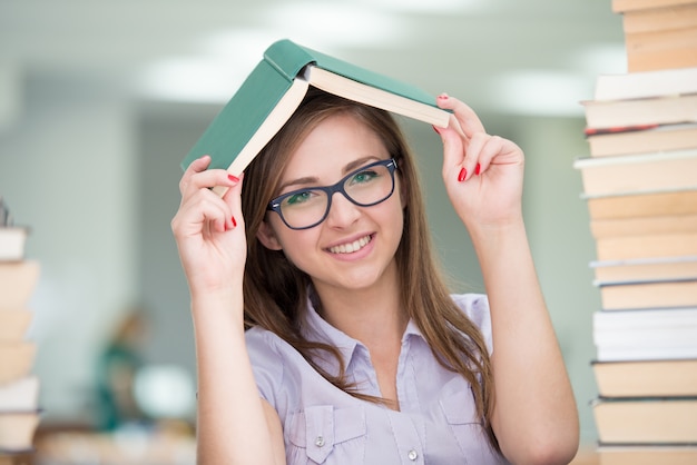 Beautiful girl studying in college library with stack of books