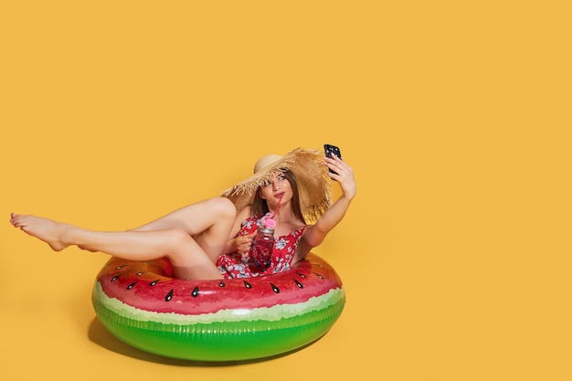 Beautiful girl in summer dress straw hat with inflatable ring shape of watermelon with fresh cocktai.