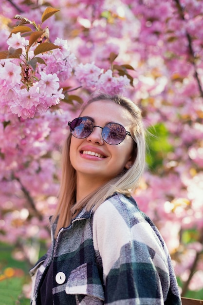 Foto bella ragazza in occhiali da sole sullo sfondo di alberi di sakura in fiore