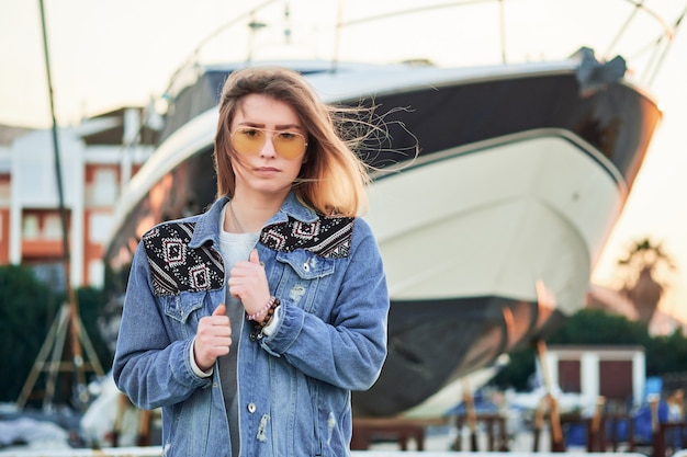 Beautiful girl in sunglasses and a denim jacket with long blonde hair in a summer sunset