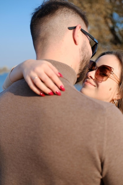 A beautiful girl in sunglasses hugs a guy by the neck and is going to kiss him