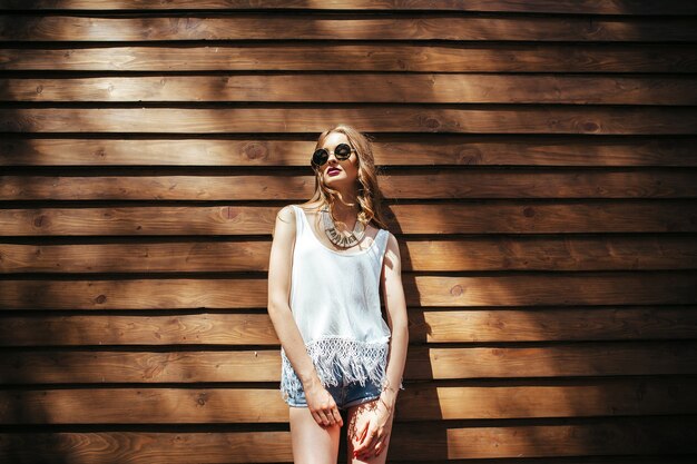 Beautiful girl in sunglasses posing on brown wall