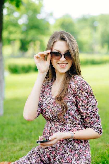 Красивая девушка в солнечных очках с телефоном отдыхает на траве в парке