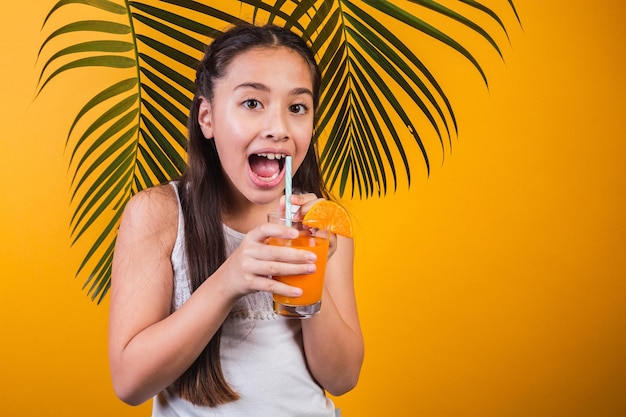 Bella ragazza sorpresa con un bicchiere di succo d'arancia su sfondo giallo.