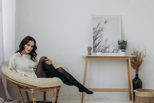 Beautiful girl in a sweater and black tights sits on an armchair