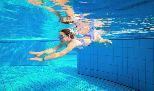 Photo beautiful girl swimming under water in blue pool wearing swimsuit and googles pretty teenager enjoying diving lessons