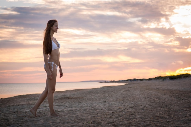 Bella ragazza in costume da bagno sulla spiaggia al tramonto