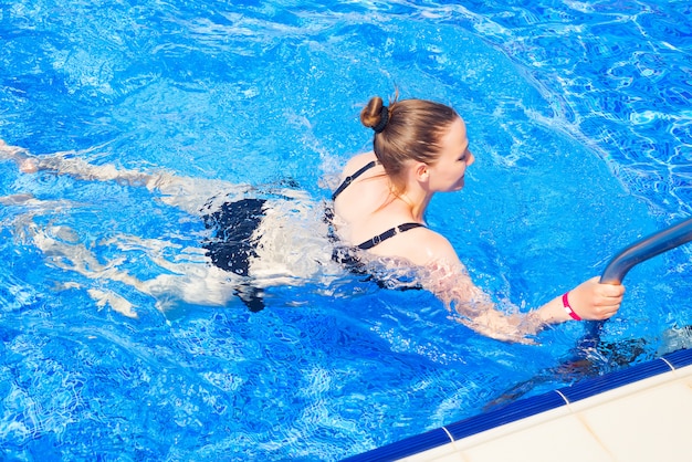 Beautiful girl in a swimsuit comes in the pool . Summer vacation