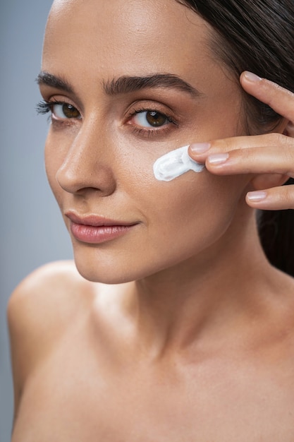beautiful girl taking care of facial skin against grey background