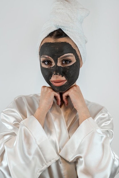 beautiful girl in towel applying black caly mask on face anti aging beauty treatment isolated