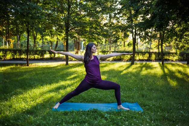 A beautiful girl in a tracksuit performs yoga exercises on a Mat at sunset on nature