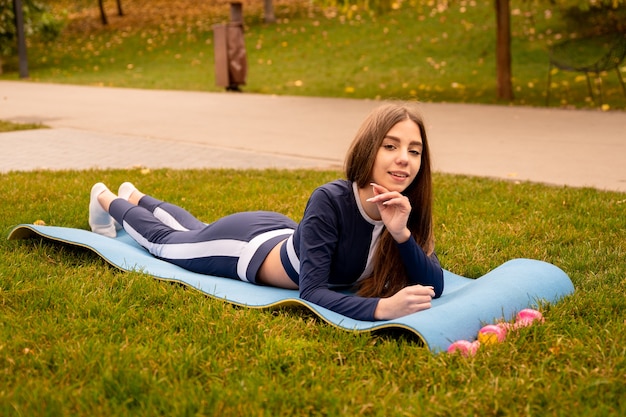 美少女トレーニング。スポーツウェアのスポーティな女の子。公園のマットの上に横たわっている女の子