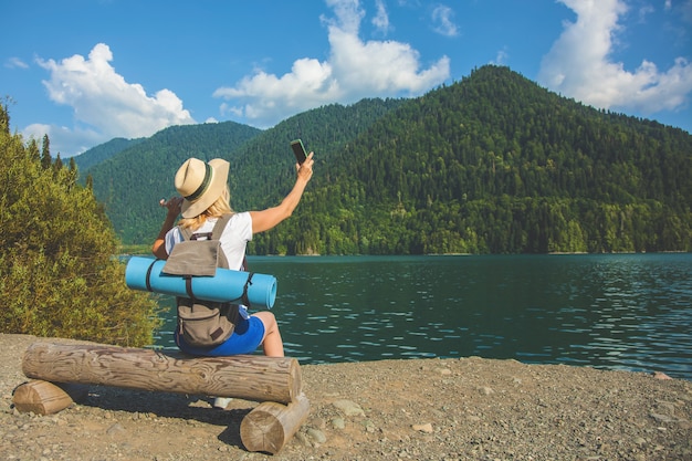 Beautiful Girl Traveler takes pictures of a large blue mountain lake in the background of the mountains