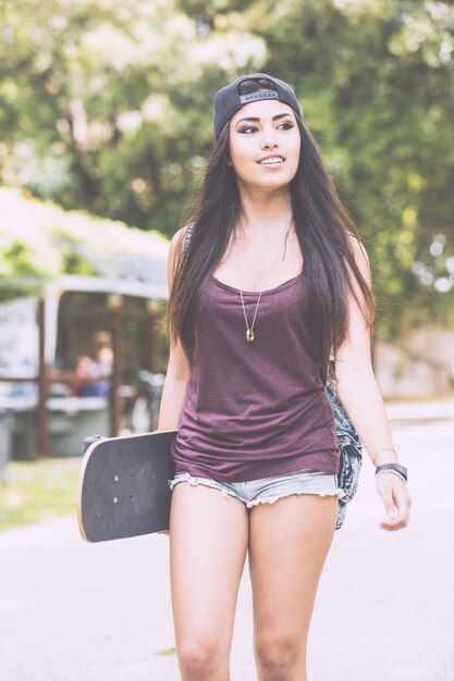 Bella ragazza che cammina al parco tenendo uno skateboard.