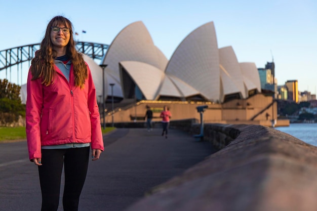 Foto bella ragazza cammina dal famoso teatro dell'opera di sydney all'alba, alba sul teatro dell'opera di sydney, aus