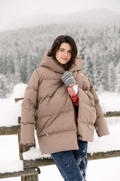 Beautiful girl walks in a snowfall. Young woman having fun in the winter forest.Outdoor portrait of pretty brunette lady posing in wood