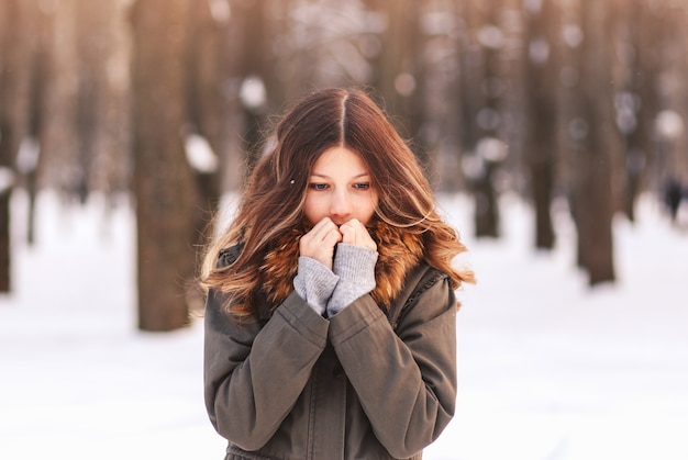 A beautiful girl warms her hands in winter on the street. Frost and sun