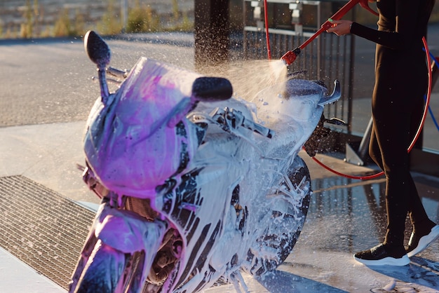 Beautiful girl washes a motorcycle at self service car wash with high pressure water