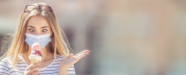 Foto bella ragazza che indossa una maschera facciale che guarda un gelato in mano con uno sguardo strabico e un gesto della mano disperato.