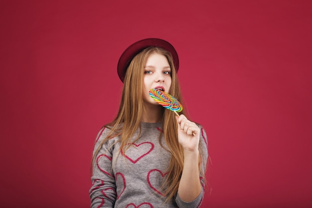 Beautiful girl wearing hat biting big striped lollipop