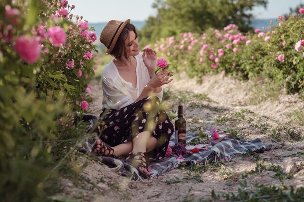 Beautiful girl wearing hat with book sitting on grass in rose gaden A country girl enjoys the sunset wine and reading books in the fragrant rose garden The concept of perfume