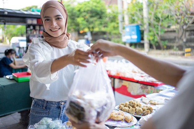 A beautiful girl wearing a headscarf selling a food stall on the side of the road gives takjil food