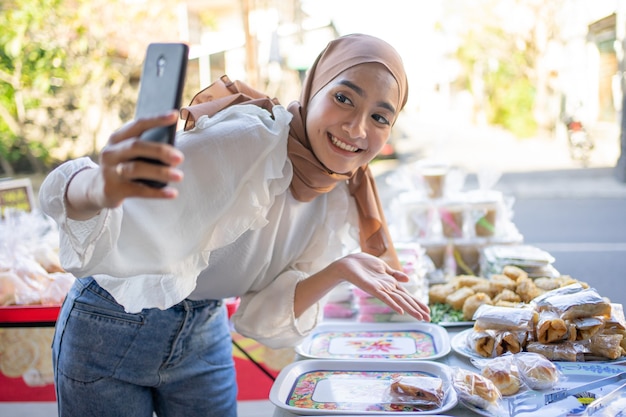 Beautiful girl wearing a smiling hijab using a mobile phone offers a variety of fried foods online